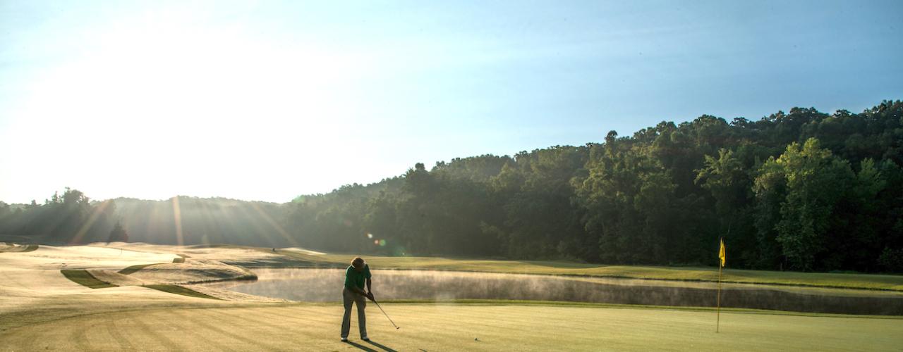 A man on the green putting towards the golf hole with the yellow flag in place