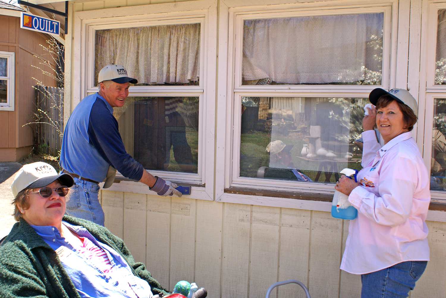 Ozark Folk Center volunteer coordinator Kathy Hair encourages volunteers Wayne and Charlotte Russell as they scrub the Spinning and Weaving Shop windows.